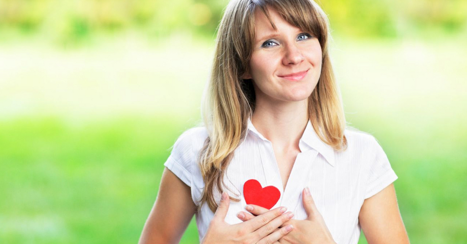 Young woman in love standing on nature holding a red paper heart Young woman in love standing on nature holding a red paper heart